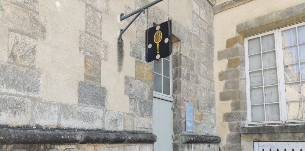 Entrée de la Salle de Jeu de Paume au Château de Fontainebleau, avec une enseigne représentant une raquette et une pancarte informative.